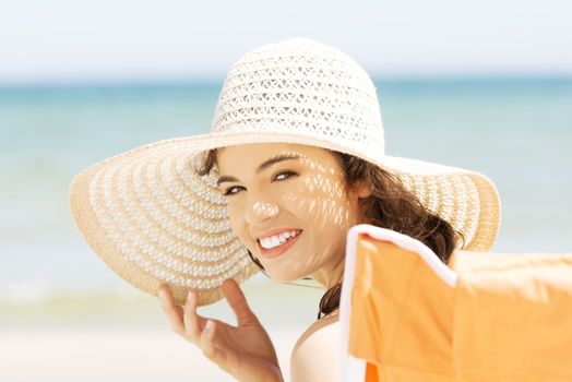 Beautiful young woman in a hat and swimsuit over seaside sunny day background.