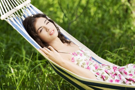 Young woman in cocktail dress relaxing in a hammock over sunny background.