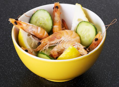 Fresh shrimps in a bowl with lemons and cucumber. Over kitchen table.
