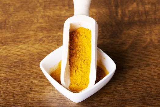 Curcuma, curry, yellow- orange spice in a bowl. Over wooden background.