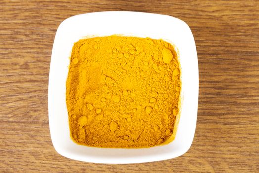 Curcuma, curry, yellow- orange spice in a bowl. Over wooden background.