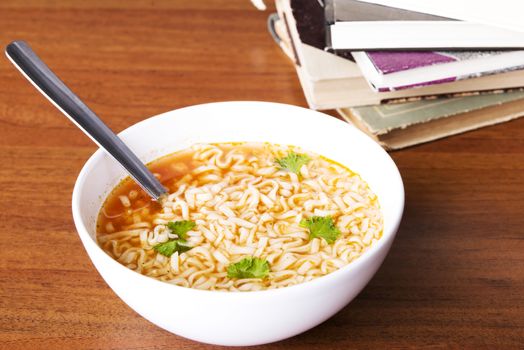 Chinese, vegetable, pasta soup next to books. On wooden table.