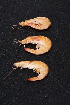 Three separated shrimps lying on a dark kitchen table.