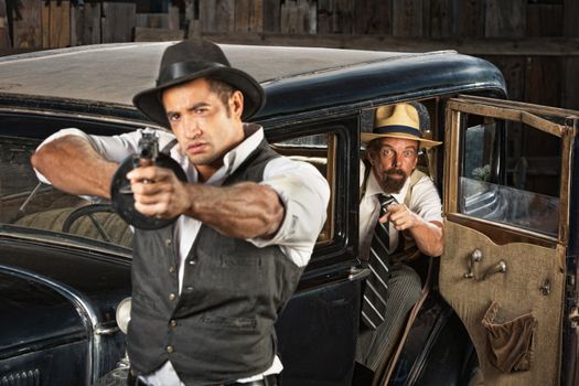 Tough 1920s vintage gangsters outside aiming guns from car