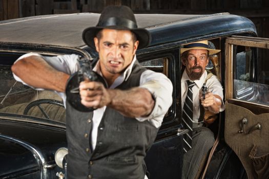 Angry 1920s vintage gangsters at car with weapons