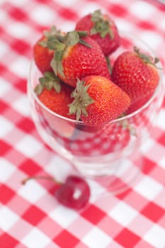 strawberry and cherry in a glass bowl on checkered fabric