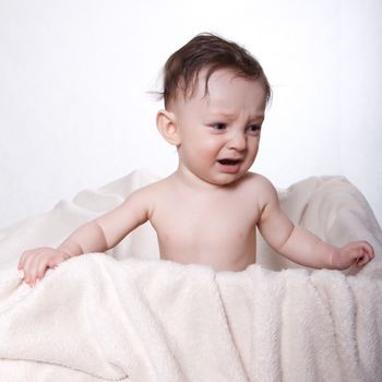 Little baby boy sitting naked on a blanket, in a box, crying, on white background
