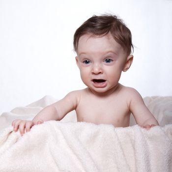 Little baby boy sitting naked on a blanket, in a box, crying, on white background