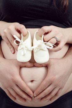 pregnant woman with a child's shoe, her husband tenderly holding her tummy with heart shape
