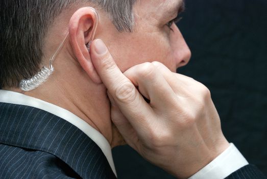 Close-up of a secret service agent listening to his earpiece, close side.