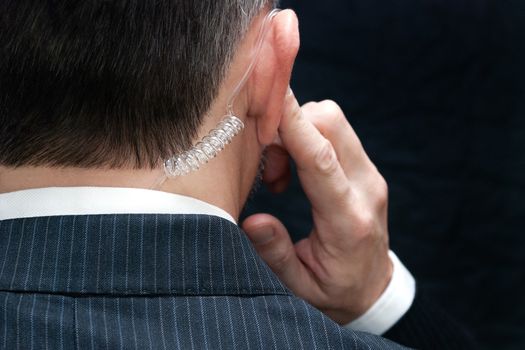 Close-up of a secret service agent listening to his earpiece, behind.