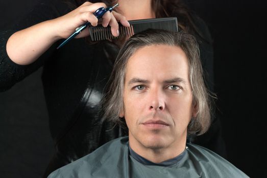 Close-up of a serious man looking to camera while his hair is combed in preparation for having it cut off for a cancer fundraiser.