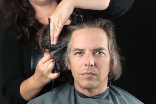 Close-up of a serious man looking to camera while his long hair is cut off for a cancer fundraiser.