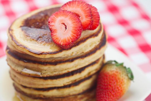 Pancakes, honey and strawberry on checkered fabric