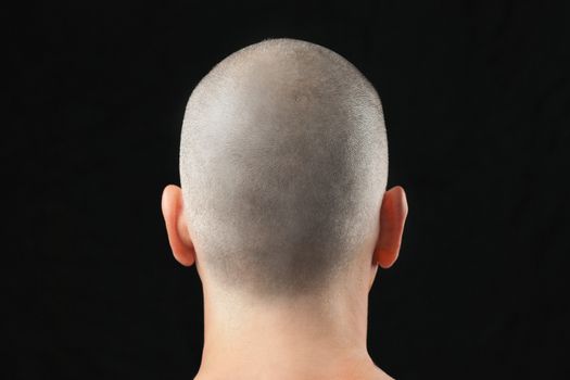 Close-up of a buddhist man with a newly shaved head, shirtless and shot from behind.