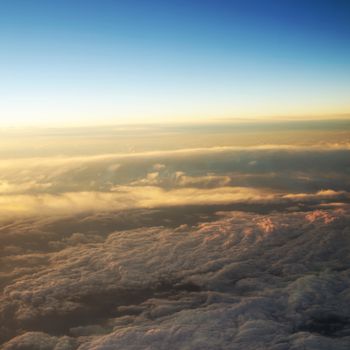 Aerial view of a cloudy sunrise while flying above the clouds. 