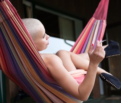 Young sensual nude woman with cigarette resting in a hammock