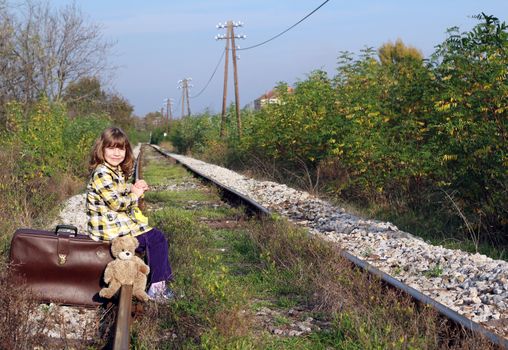 little girl sitting on suitcase and waiting for train