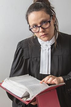 thirty something brunette woman wearing a canadian lawyer toga with a red criminal law book in hand looking over her glasses
