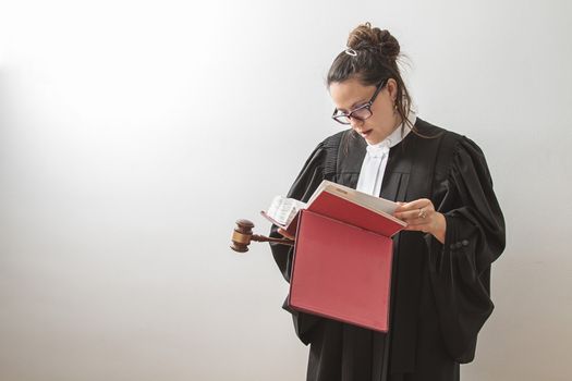 thirty something brunette woman wearing a canadian lawyer toga with a gavel in her hands and reading a red criminal law book