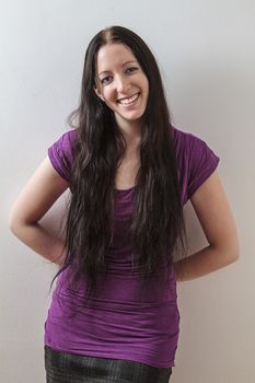 young woman with long black hair and a purple shirt, leaning on a wall with her hand on her back