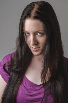 young woman with long black hair and a purple shirt, with her head down and looking up from the corner of her eyes