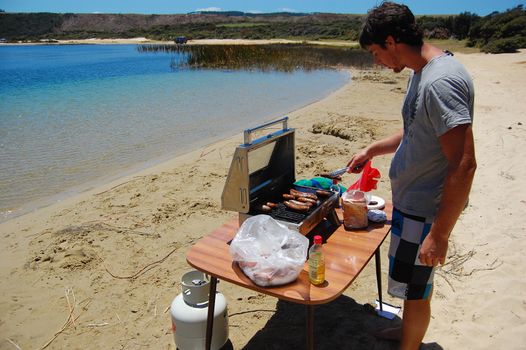 Man cooking sausages at barbeque in beach, New Zealand