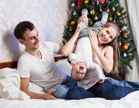 Young family with a baby having fun on bed at home