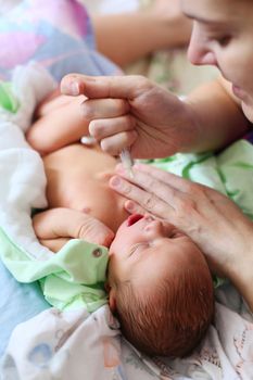 Mother feeding newborn baby milk with syringe at home