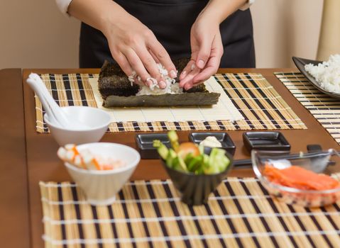 Hands of woman chef filling japanese sushi rolls with rice on a nori seaweed sheet. Selective focus in sushi roll.