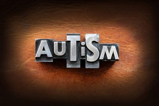 The word Autism made from vintage lead letterpress type on a leather background.