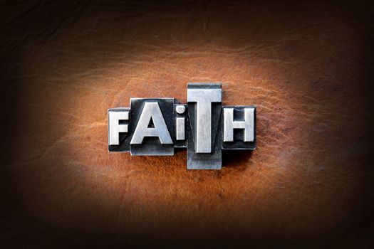 The word faith made from vintage lead letterpress type on a leather background.