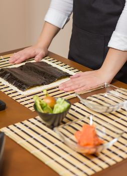 Woman chef ready to prepare japanese sushi rolls, with principal ingredients in the foreground. Selective focus in nori seaweed.