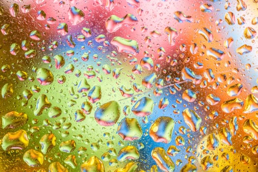 A bright colorful background image of water droplets on a glass surface