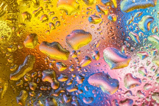 A bright colorful background image of water droplets on a glass surface