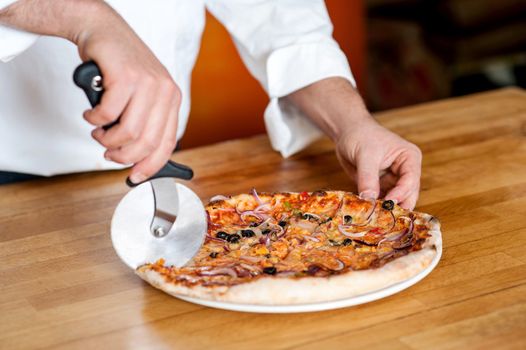 Closeup shot of male chef cutting pizza before delivery