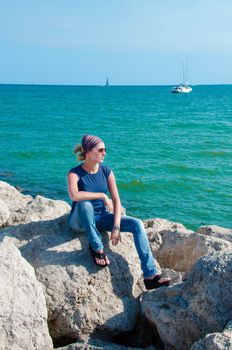 Beautiful young woman sitting on the stone on the seashore