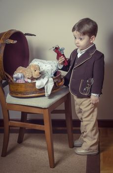 Vintage portrait of cute little boy playing with antique tin toys found in a old case. Retro style concept.