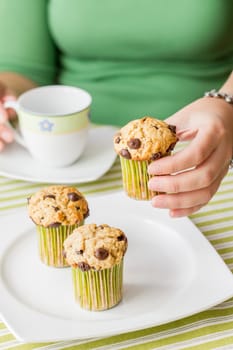 Nice girl hand taking delicious chocolate chip muffin at breakfast in green striped tablecloth