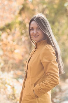 Woman is walking in autumnal park in yellow coat