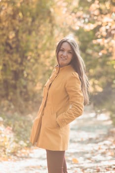 Woman is walking in autumnal park in yellow coat