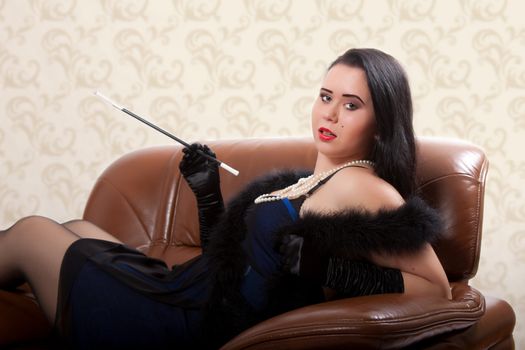 Young woman in retro clothing lying in a big chair with a cigarette holder