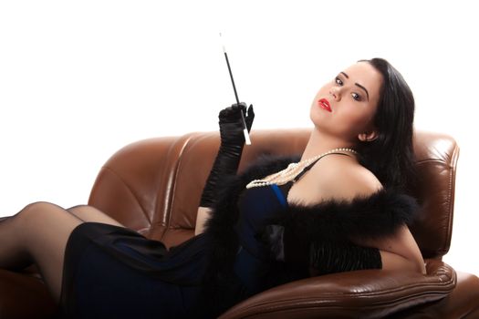 Young woman in retro clothing lying in a big chair with a cigarette holder, on white background