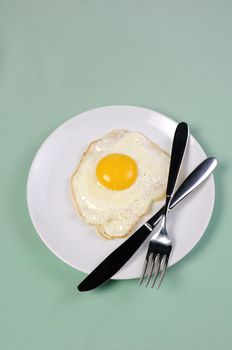 Fried eggs on a white plate with knife and fork