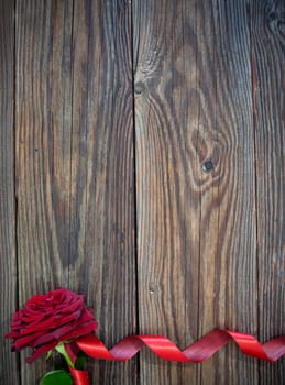 Red rose with decorative ribbon border over a wooden background 