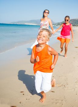 Adorable happy boy with sister and mother running on beach