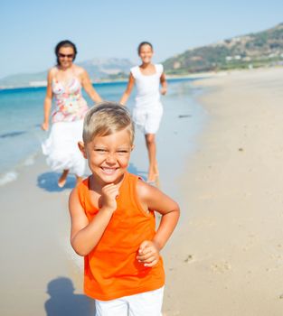 Adorable happy boy with sister and mother running on beach