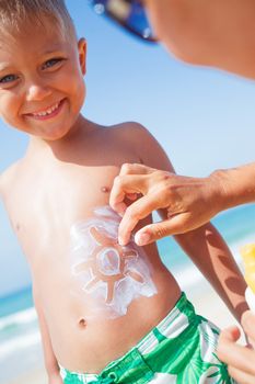 Adorable boy and mother at tropical beach applying sunblock cream.