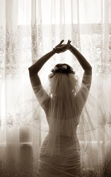 The beautiful bride prepares for wedding. Silhouette on a background of a window