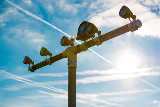 Runway lights at the airport in front of a great blue sky with clouds, bright sunlight and vapor trails